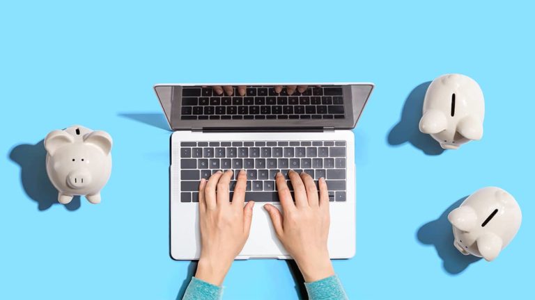 person typing on a laptop surrounded by piggy banks